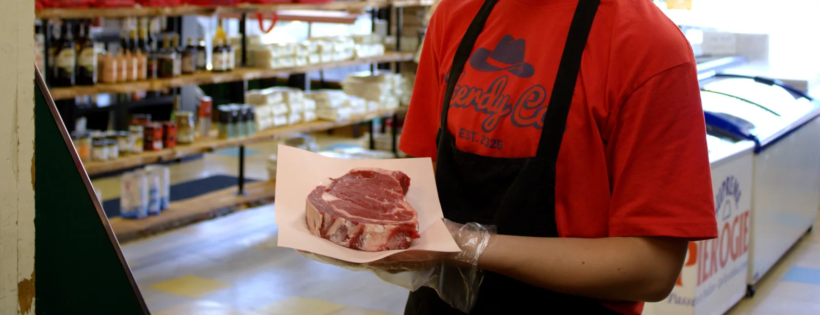 A Herdy Co. butcher holding a freshly cut steak behind the counter